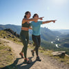 Two women on a mountain trail pointing towards a scenic view