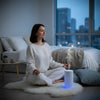 Woman meditating in a bedroom with a diffuser emitting mist.